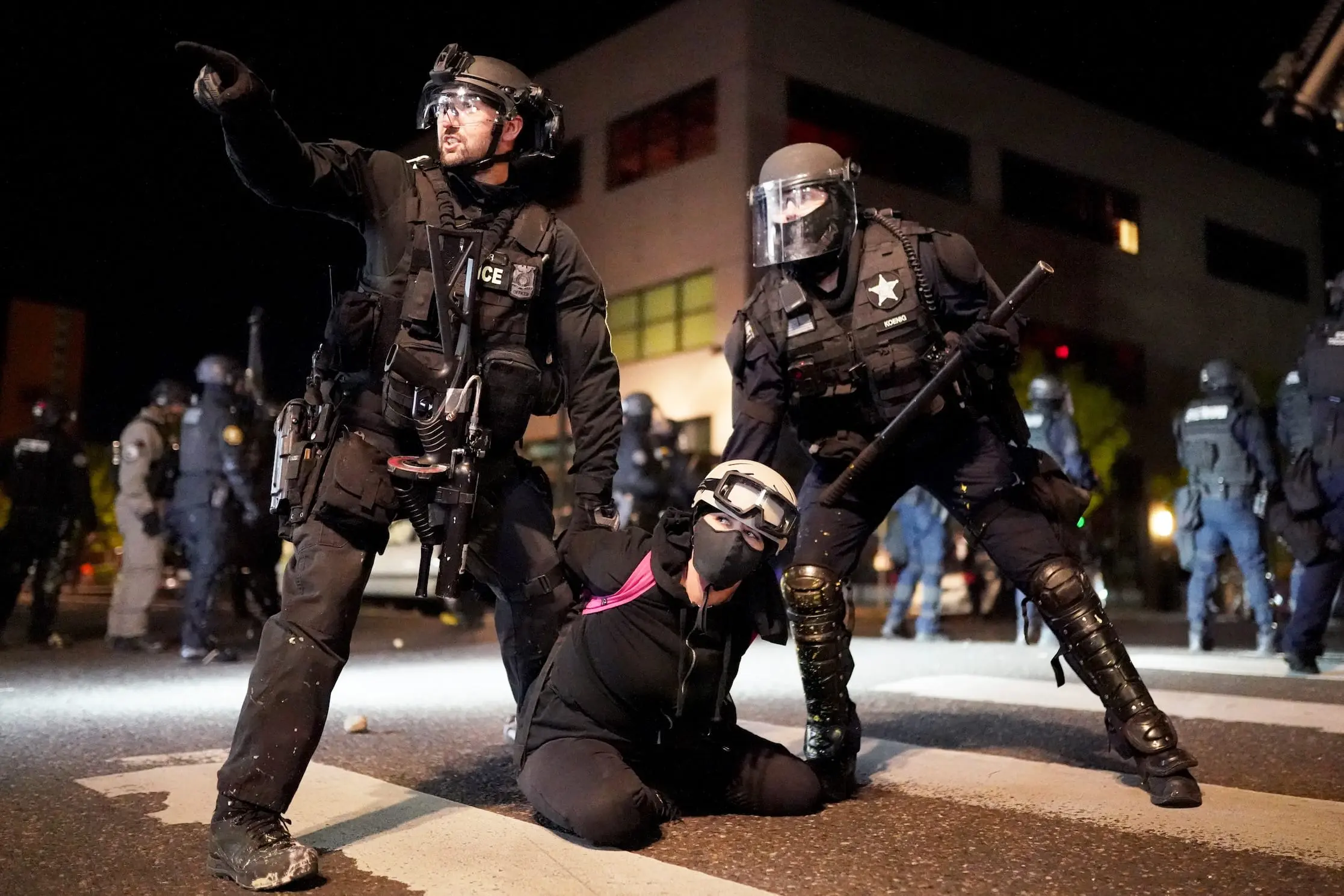 Two police officers detain a woman in the middle of the street at night.